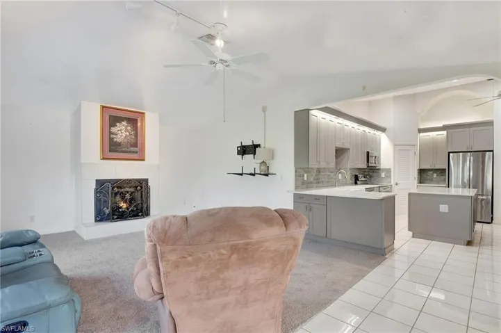 Living room featuring light carpet, vaulted ceiling, ceiling fan, and a fireplace