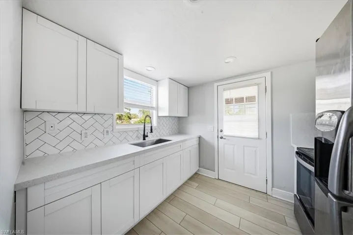 Kitchen featuring stainless steel appliances, white cabinets, light stone counters, light wood-style floors, and backsplash
