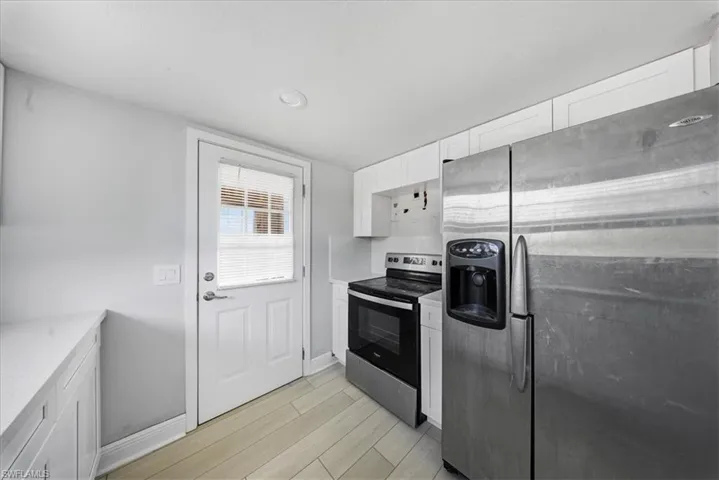 Kitchen with appliances with stainless steel finishes, white cabinets, light wood-style flooring, and light stone countertops