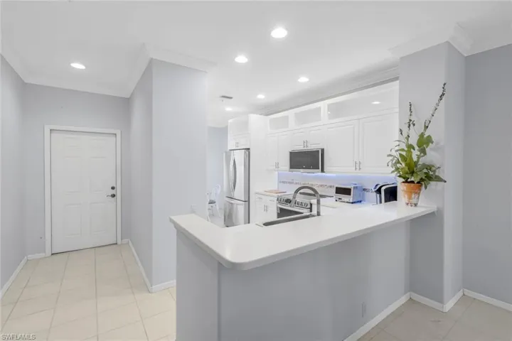 Kitchen with white cabinets, light tile patterned floors, light countertops, glass insert cabinets, and a peninsula