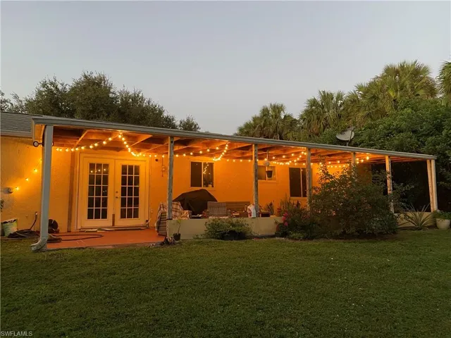 Rear view of property with french doors, a patio, a lawn, and stucco siding