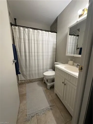 Full bathroom with toilet, tile patterned floors, curtained shower, and vanity
