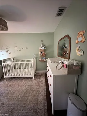 Bedroom featuring a nursery area, visible vents, baseboards, and dark colored carpet