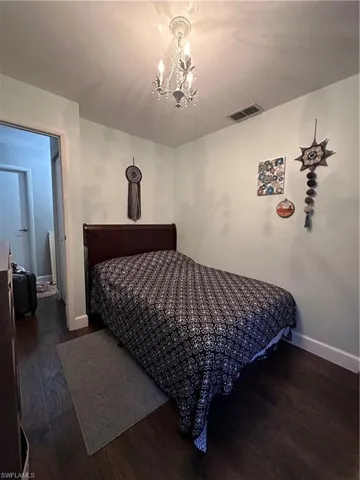 Bedroom with a notable chandelier, visible vents, baseboards, and wood finished floors