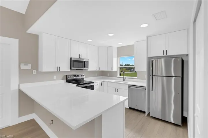 Modern kitchen featuring white cabinetry, light countertops, stainless steel appliances, and wood-finish flooring