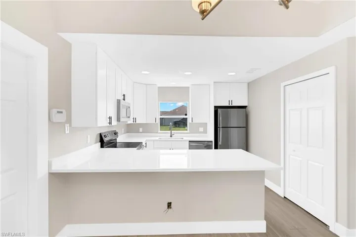 Modern kitchen featuring a large white countertop, white cabinetry with black hardware, and dark wood-finish flooring