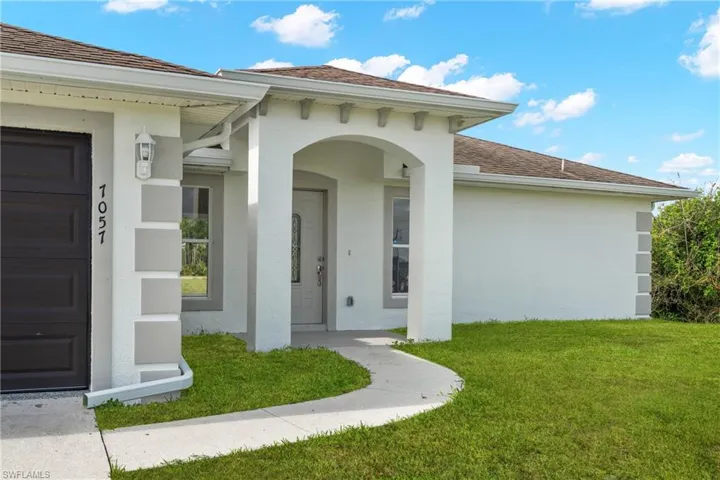 Contemporary exterior featuring a covered entry porch with arched detailing, a gray front door with decorative glass, and a dark brown garage door