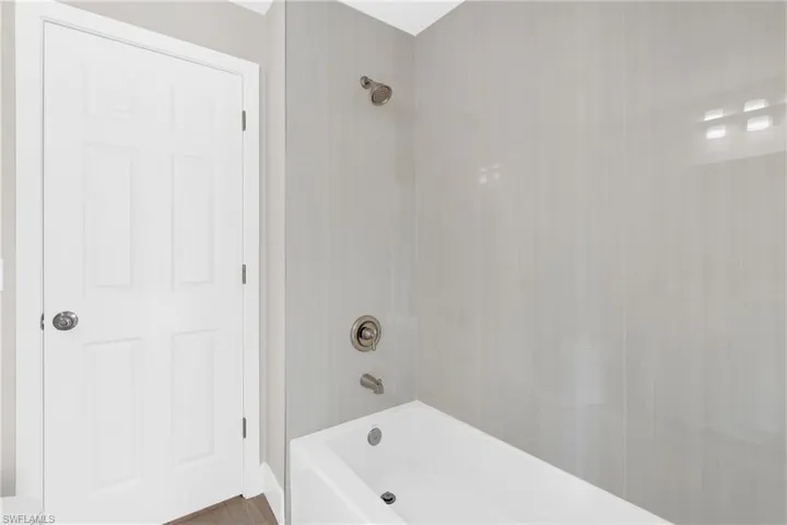 Bathtub with brushed nickel fixtures and light gray tiled surround
