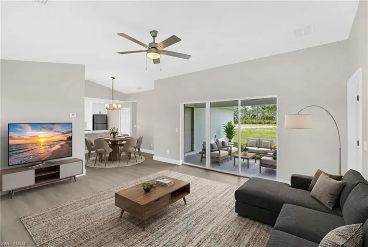 Virtually Staged.  Open-concept living area featuring vaulted ceilings, wood-finish flooring, a ceiling fan, and sliding glass doors opening to an outdoor patio