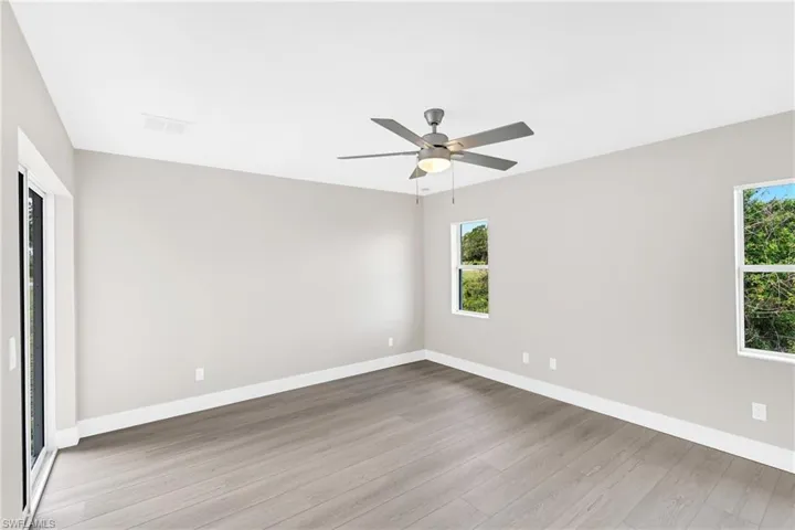 Spacious room featuring wood-finish flooring, light gray walls, white baseboards, and a contemporary ceiling fan with integrated lighting