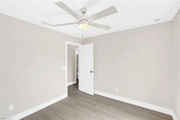 Room featuring wood-finish flooring, light gray walls, white trim, and a ceiling fan with integrated lighting