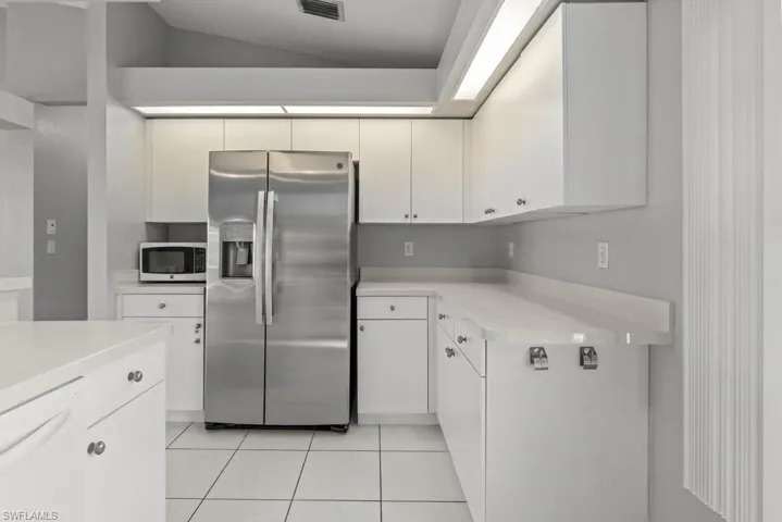 Kitchen featuring stainless steel fridge with ice dispenser, dishwasher, white cabinetry, light tile patterned floors, and vaulted ceiling