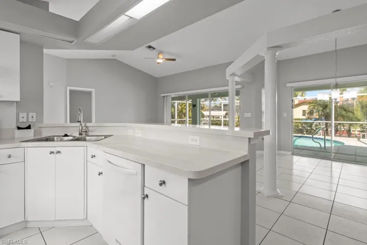 Kitchen featuring a peninsula, light tile patterned flooring, vaulted ceiling, light countertops, and dishwasher