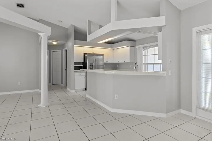 Kitchen with light countertops, a peninsula, stainless steel fridge, ornate columns, and light tile patterned floors