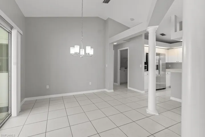 Unfurnished dining area with ornate columns, vaulted ceiling, light tile patterned floors, and hanging lights