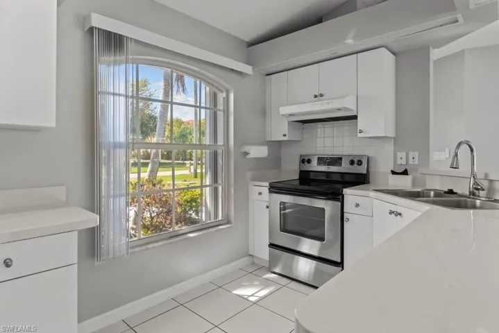 Kitchen with electric stove, light countertops, tasteful backsplash, white cabinetry, and light tile patterned floors