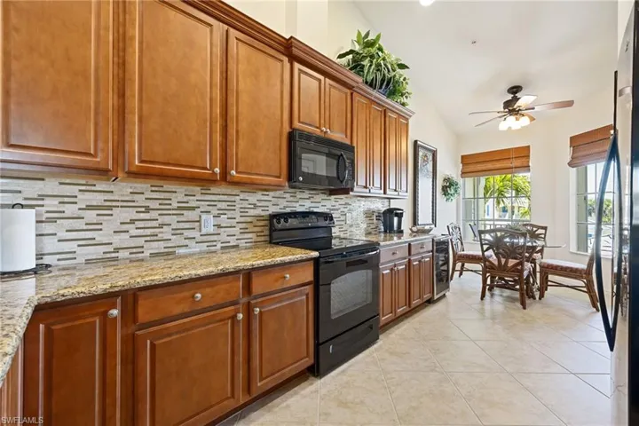 Kitchen featuring black appliances, a ceiling fan, beverage cooler, light stone countertops, and light tile patterned flooring