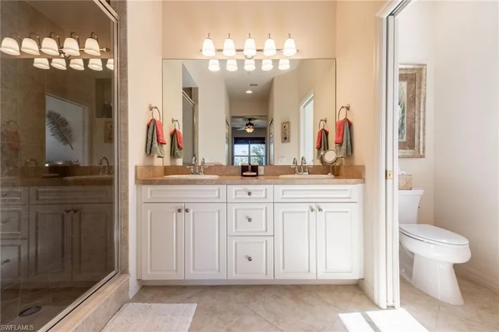 Bathroom with double vanity, a shower stall, light tile patterned floors, and ceiling fan