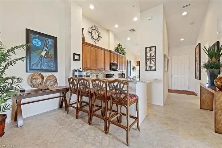Kitchen featuring a kitchen bar, wood finish cabinets, a peninsula, tasteful backsplash, and light stone counters
