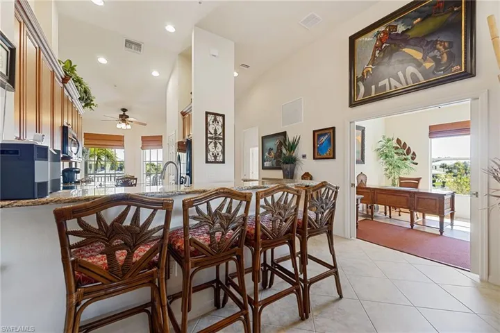 Kitchen featuring a breakfast bar area, ceiling fan, a high ceiling, light stone countertops, and stainless steel appliances