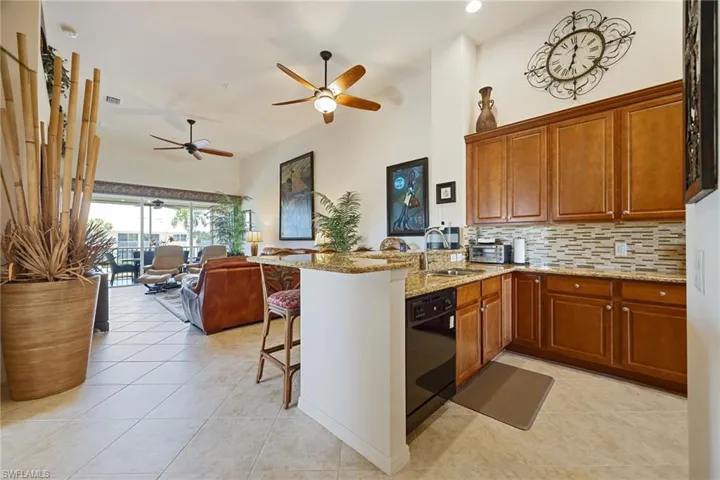 Kitchen featuring a peninsula, a kitchen breakfast bar, light stone countertops, a high ceiling, and tasteful backsplash