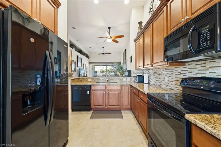 Kitchen featuring black appliances, light stone counters, wood finish cabinets, decorative backsplash, and recessed lighting