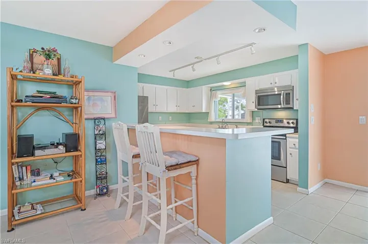 Kitchen featuring light countertops, a kitchen bar, white cabinetry, stainless steel appliances, and light tile patterned flooring