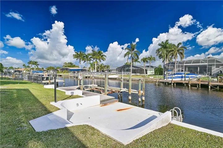 Dock featuring boat lift, a lawn, a water view, and a residential view