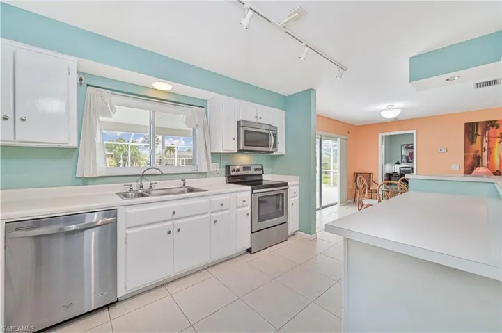 Kitchen featuring track lighting, appliances with stainless steel finishes, white cabinets, and healthy amount of natural light