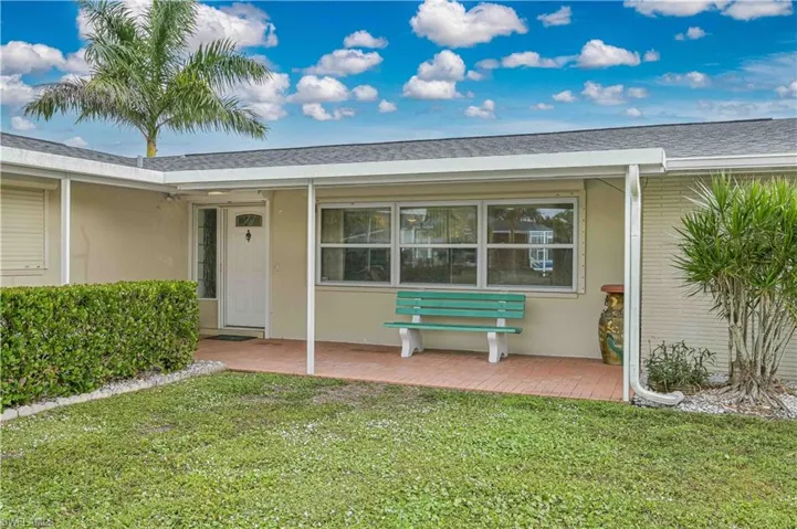 Property entrance with a lawn, stucco siding, roof with shingles, and a patio area