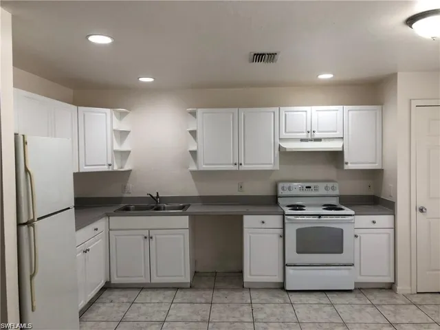 Kitchen featuring white appliances, white cabinets, open shelves, under cabinet range hood, and dark countertops
