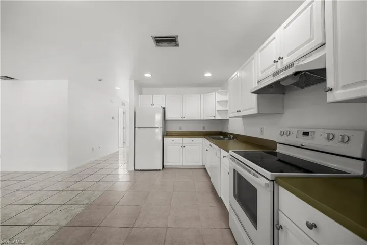 Kitchen featuring white appliances, dark countertops, under cabinet range hood, recessed lighting, and white cabinets
