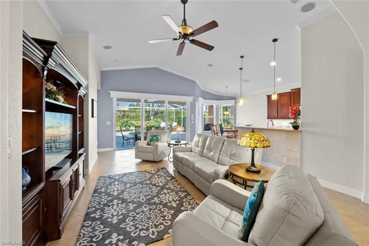 Living area with light tile patterned floors, lofted ceiling, ceiling fan, and crown molding