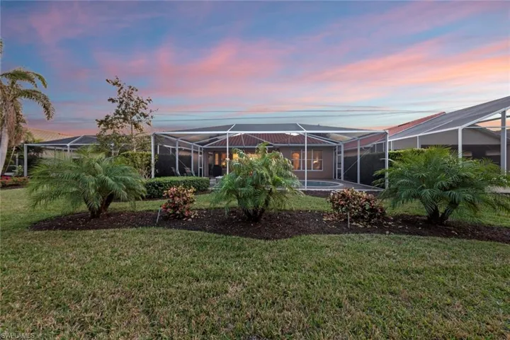 Back house at dusk with glass enclosure and a lawn