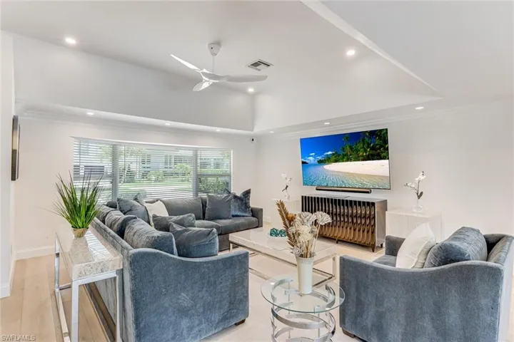 Spacious living area featuring light wood-finish flooring, recessed lighting, and a vaulted ceiling with a white ceiling fan