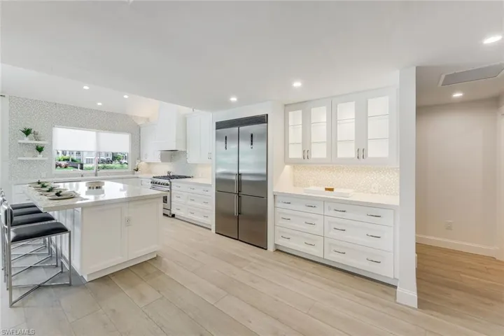 Bright kitchen featuring white cabinetry, a large center island with seating, stainless steel appliances, and wood-finish flooring