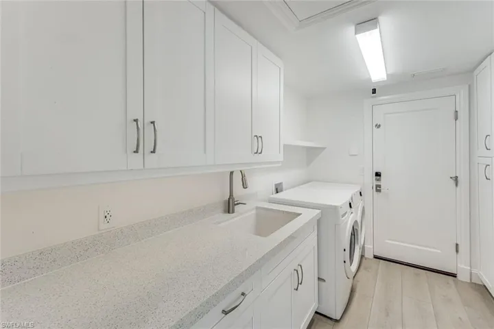 Laundry area featuring white shaker-style cabinetry, a built-in sink, and speckled stone-finish countertops