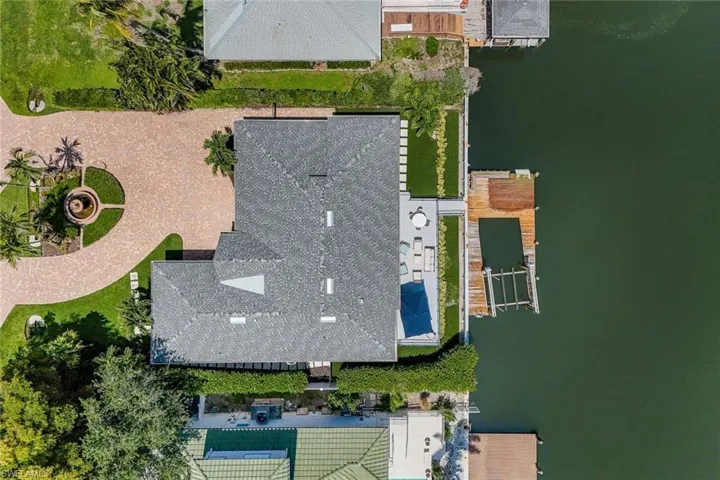 Waterfront property featuring a private boat dock, paved drive with circular fountain, manicured lawn, paved patio, and mature landscaping