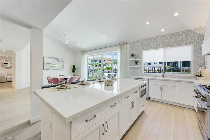 Spacious kitchen featuring a large island with a light-colored countertop, white cabinetry with dark pulls, wood-finish flooring, recessed lighting, and a window with a water feature backdrop