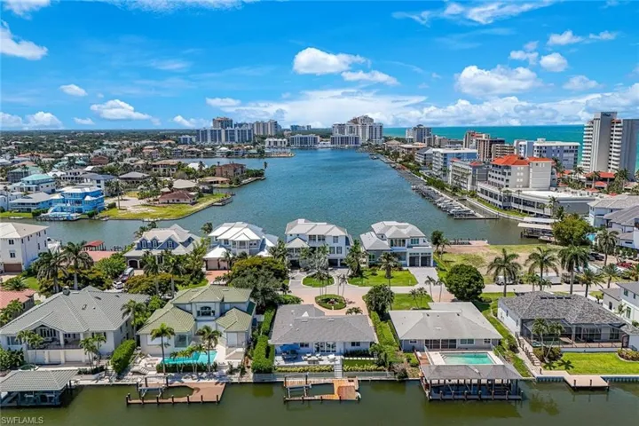 Waterfront community featuring an extensive canal system with private docks, a variety of architectural styles, mature palm trees, and distant high-rise buildings