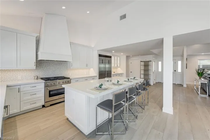 Open-concept kitchen featuring white shaker cabinetry, an integrated range hood, stainless steel appliances, a center island with seating, and wood-finish flooring