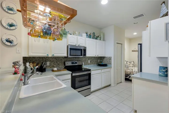 Kitchen featuring appliances with stainless steel finishes, white cabinetry, tasteful backsplash, sink, and light tile patterned floors