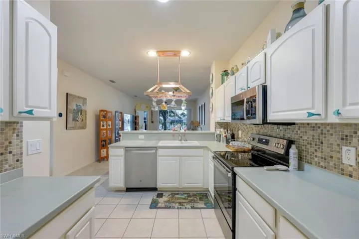 Kitchen featuring white cabinets, appliances with stainless steel finishes, tasteful backsplash, and pendant lighting
