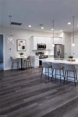 Kitchen with a kitchen bar, hanging light fixtures, white cabinetry, stainless steel appliances, and dark wood finished floors