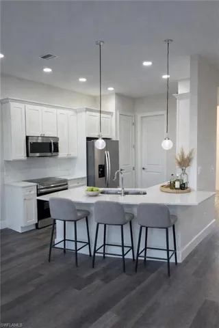 Kitchen with stainless steel appliances, a kitchen bar, white cabinets, a peninsula, and dark wood-type flooring