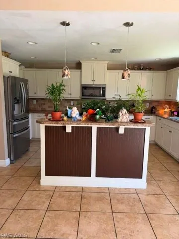 Kitchen featuring a kitchen island, light stone countertops, fridge, light tile patterned floors, and tasteful backsplash