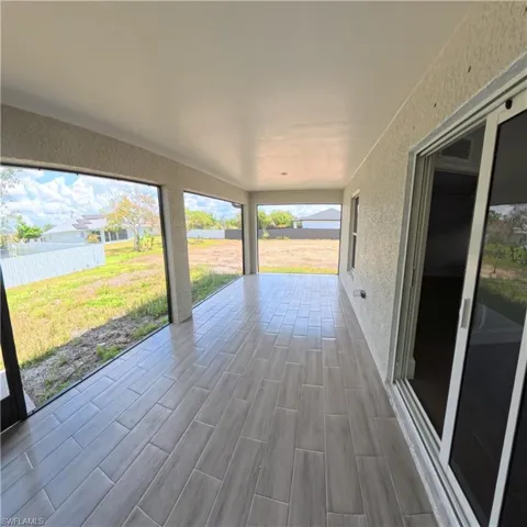 Spacious screened patio featuring light gray plank-style tile flooring, a textured stucco exterior wall, and sliding glass doors