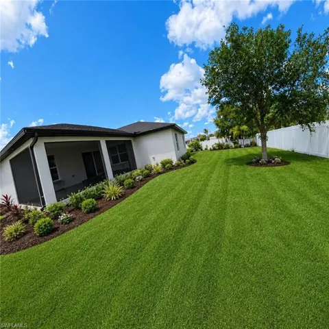 Expansive backyard featuring a manicured lawn, established tree, and white privacy fencing