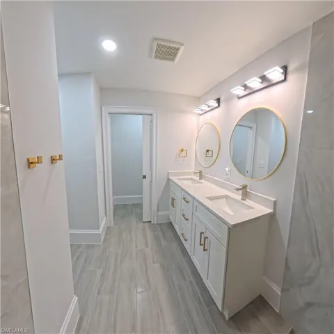 Double vanity featuring white cabinetry with gold-tone hardware, two undermount sinks, and light-toned countertops