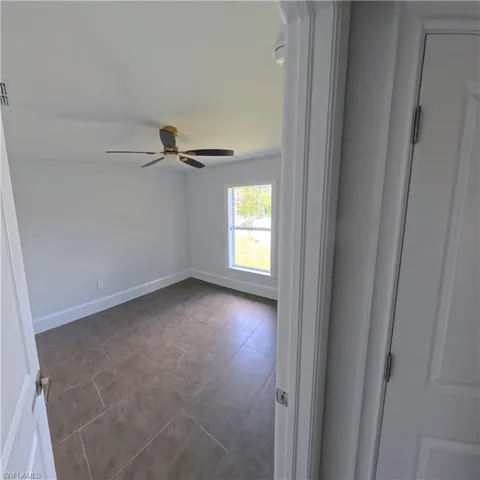 Bright room featuring large format tile flooring, a prominent window, a ceiling fan with light fixture, and white trim throughout